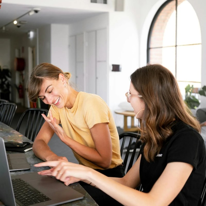 Two woman laughing and discussing whats on a laptop screen.