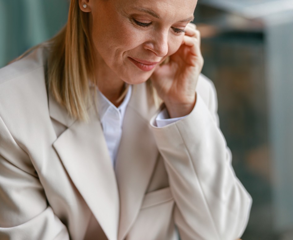 A business woman with a hand to her head, looking downwards at floorplans.